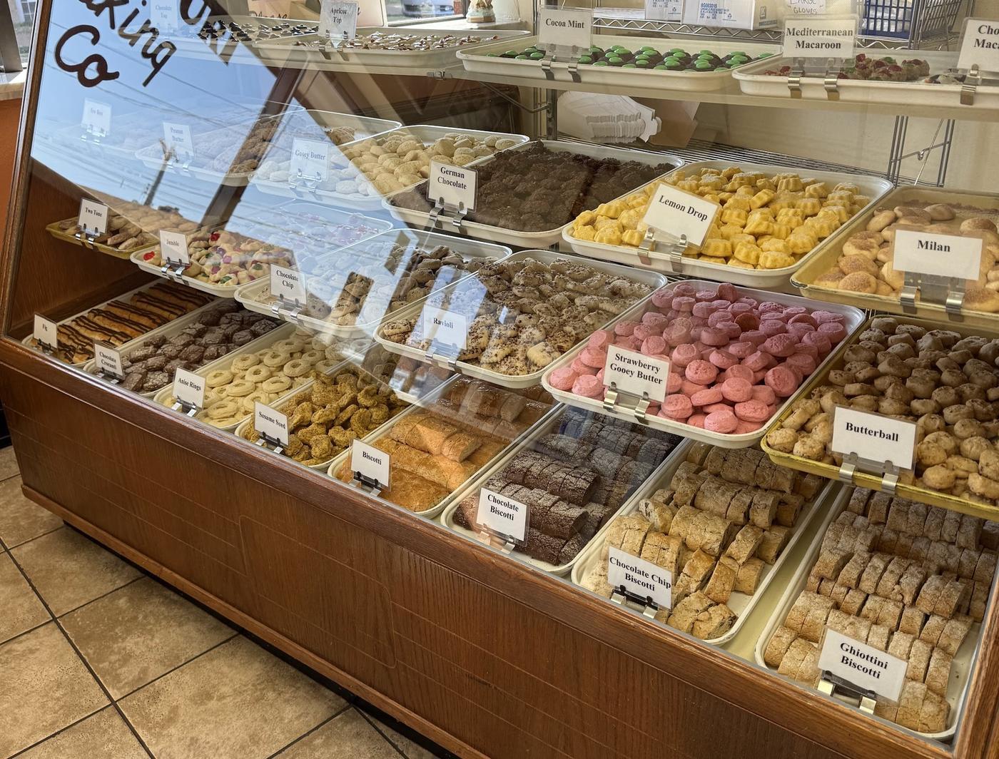 The cookie case at Missouri Baking Co, every tray labelled by name: butterball, anise rings, lemon drop, strawberry gooey butter, chocolate chip biscotti and more